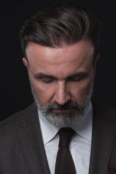 Portrait of a stylish elegant senior businessman with a beard and casual business clothes in photo studio isolated on dark background gesturing with hands. High quality photo