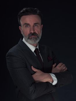 Portrait of a stylish elegant senior businessman with a beard and casual business clothes in photo studio isolated on dark background gesturing with hands. High quality photo