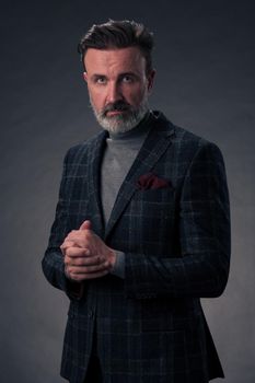 Portrait of a stylish elegant senior businessman with a beard and casual business clothes in photo studio isolated on dark background gesturing with hands. High quality photo