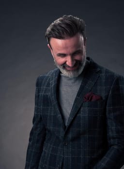 Portrait of a stylish elegant senior businessman with a beard and casual business clothes in photo studio isolated on dark background gesturing with hands. High quality photo