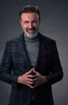 Portrait of a stylish elegant senior businessman with a beard and casual business clothes in photo studio isolated on dark background gesturing with hands. High quality photo