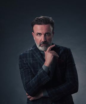 Portrait of a stylish elegant senior businessman with a beard and casual business clothes in photo studio isolated on dark background gesturing with hands. High quality photo