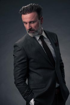 Portrait of a stylish elegant senior businessman with a beard and casual business clothes in photo studio isolated on dark background gesturing with hands. High quality photo