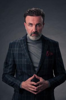 Portrait of a stylish elegant senior businessman with a beard and casual business clothes in photo studio isolated on dark background gesturing with hands. High quality photo