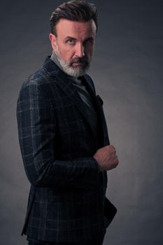 Portrait of a stylish elegant senior businessman with a beard and casual business clothes in photo studio isolated on dark background gesturing with hands. High quality photo