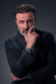 Portrait of a stylish elegant senior businessman with a beard and casual business clothes in photo studio isolated on dark background gesturing with hands. High quality photo