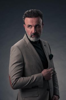 Portrait of a stylish elegant senior businessman with a beard and casual business clothes in photo studio isolated on dark background gesturing with hands. High quality photo