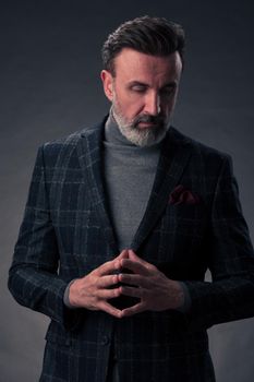 Portrait of a stylish elegant senior businessman with a beard and casual business clothes in photo studio isolated on dark background gesturing with hands. High quality photo