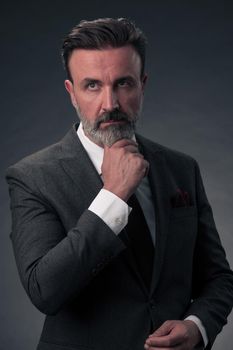 Portrait of a stylish elegant senior businessman with a beard and casual business clothes in photo studio isolated on dark background gesturing with hands. High quality photo