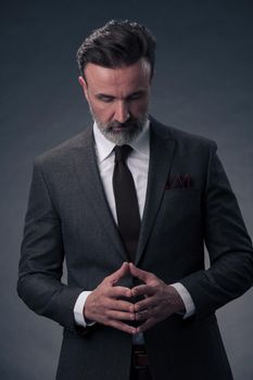 Portrait of a stylish elegant senior businessman with a beard and casual business clothes in photo studio isolated on dark background gesturing with hands. High quality photo