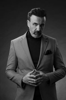 Portrait of a stylish elegant senior businessman with a beard and casual business clothes in photo studio isolated on dark background gesturing with hands. High quality photo