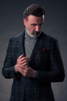 Portrait of a stylish elegant senior businessman with a beard and casual business clothes in photo studio isolated on dark background gesturing with hands. High quality photo