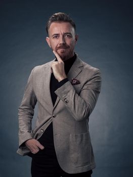 Portrait of a stylish elegant senior businessman with a beard and casual business clothes in photo studio isolated on dark background gesturing with hands. High quality photo