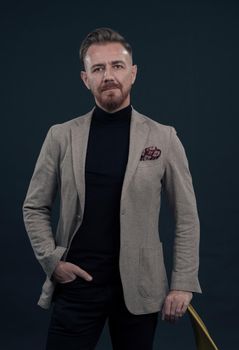 Portrait of adult businessman wearing trendy suit and sitting in modern studio on stylish chair against the black background. Horizontal mockup. High quality photo