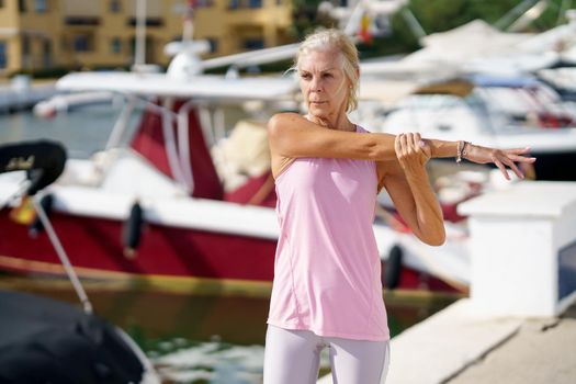 Mature sportswoman stretching her shoulders after exercise. Concept of healthy living in the elderly. Senior woman in fitness clothing. Older female doing sport to keep fit.