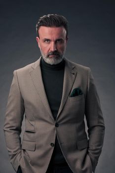 Portrait of a stylish elegant senior businessman with a beard and casual business clothes in photo studio isolated on dark background gesturing with hands. High quality photo