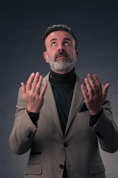 Portrait of a stylish elegant senior businessman with a beard and casual business clothes in photo studio isolated on dark background gesturing with hands. High quality photo