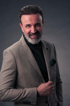 Portrait of a stylish elegant senior businessman with a beard and casual business clothes in photo studio isolated on dark background gesturing with hands. High quality photo