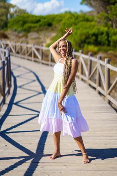 African female wearing a beautiful dress on a boardwalk on the beach. Fashion woman outdoors.