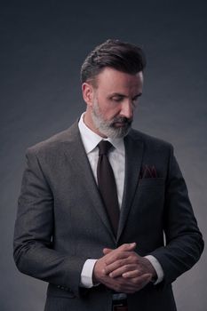 Portrait of a stylish elegant senior businessman with a beard and casual business clothes in photo studio isolated on dark background gesturing with hands. High quality photo