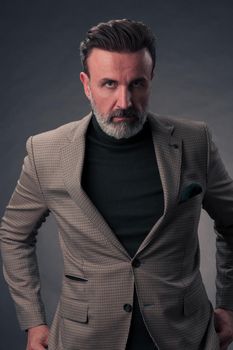 Portrait of a stylish elegant senior businessman with a beard and casual business clothes in photo studio isolated on dark background gesturing with hands. High quality photo