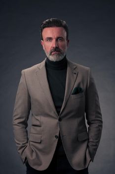 Portrait of a stylish elegant senior businessman with a beard and casual business clothes in photo studio isolated on dark background gesturing with hands. High quality photo