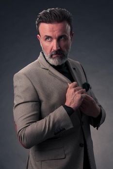 Portrait of a stylish elegant senior businessman with a beard and casual business clothes in photo studio isolated on dark background gesturing with hands. High quality photo