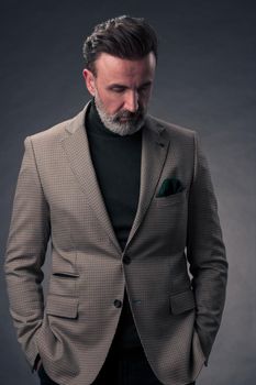 Portrait of a stylish elegant senior businessman with a beard and casual business clothes in photo studio isolated on dark background gesturing with hands. High quality photo