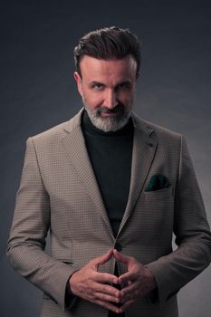 Portrait of a stylish elegant senior businessman with a beard and casual business clothes in photo studio isolated on dark background gesturing with hands. High quality photo