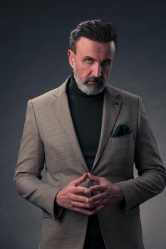 Portrait of a stylish elegant senior businessman with a beard and casual business clothes in photo studio isolated on dark background gesturing with hands. High quality photo