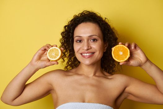 Young woman with a beautiful smile holding halves of orange and lemon near her face. Concepts, healthy eating, skin and body care. Yellow background, copy space