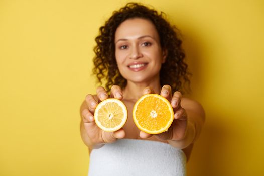 Soft focus on slices of citrus , lemon and orange, in the hands of a blurry smiling mixed race and curly-haired woman, isolated over yellow background with space for text