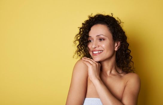 Attractive African American young woman with curly hair looking away and smiling with toothy smile. Yellow background. Copy space for promotion