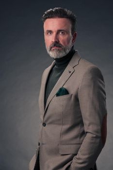 Portrait of a stylish elegant senior businessman with a beard and casual business clothes in photo studio isolated on dark background gesturing with hands. High quality photo