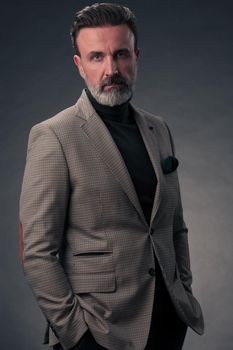 Portrait of a stylish elegant senior businessman with a beard and casual business clothes in photo studio isolated on dark background gesturing with hands. High quality photo