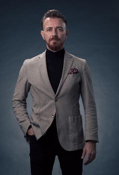 Portrait of a stylish elegant senior businessman with a beard and casual business clothes in photo studio isolated on dark background gesturing with hands. High quality photo