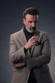 Portrait of a stylish elegant senior businessman with a beard and casual business clothes in photo studio isolated on dark background gesturing with hands. High quality photo