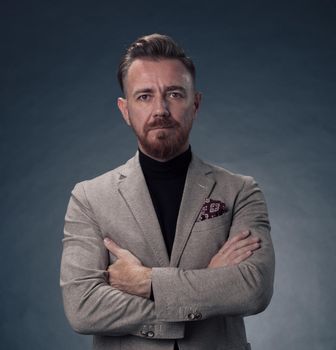 Portrait of a stylish elegant senior businessman with a beard and casual business clothes in photo studio isolated on dark background gesturing with hands. High quality photo