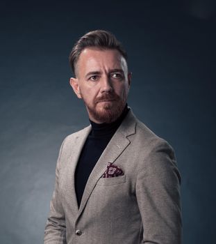 Portrait of a stylish elegant senior businessman with a beard and casual business clothes in photo studio isolated on dark background gesturing with hands. High quality photo