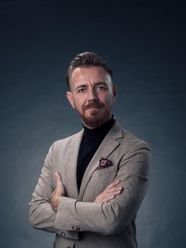 Portrait of a stylish elegant senior businessman with a beard and casual business clothes in photo studio isolated on dark background gesturing with hands. High quality photo