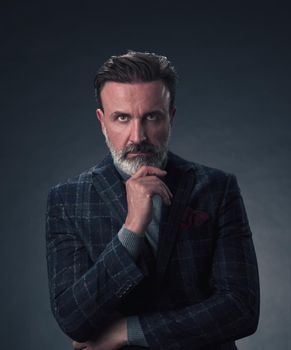 Portrait of a stylish elegant senior businessman with a beard and casual business clothes in photo studio isolated on dark background gesturing with hands. High quality photo