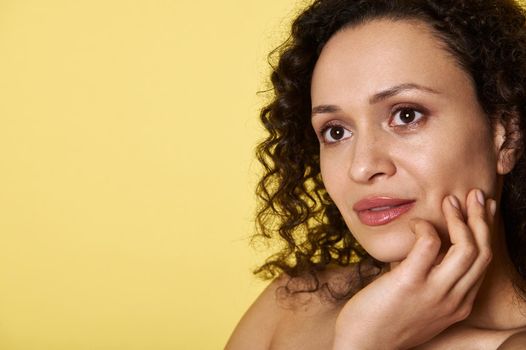 Close Up portrait of a pretty woman with curly hair looking dreamily away isolated on yellow background with copy space