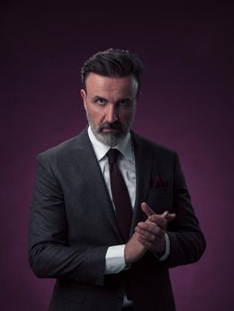 Portrait of a stylish elegant senior businessman with a beard and casual business clothes in photo studio isolated on dark background gesturing with hands. High quality photo