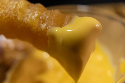 Close-up of melted cheddar cheese on wavy French fry above blurry background. Fried potato snack covered with tasty yellow dip. Delicious fast food preparation