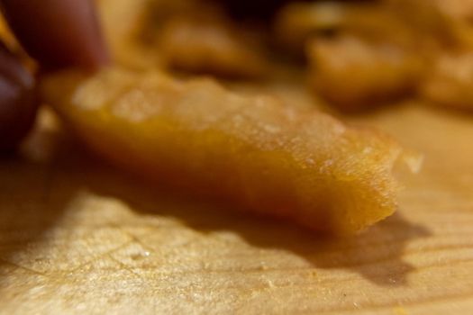 Extreme close-up of fingers grabbing wavy French fry on wooden surface. Small pile of tasty fried potato snacks with crunchy texture. Delicious fast food preparation