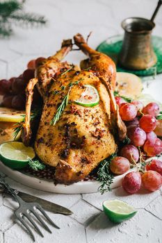 A duck baked for Thanksgiving as a symbol of family unification at a common holiday table. Still life in orange tones, shot in a light key on a white ceramic background. The atmosphere of the festival and celebration. The dish is decorated with grapes, lime, quince and aromatic herbs.