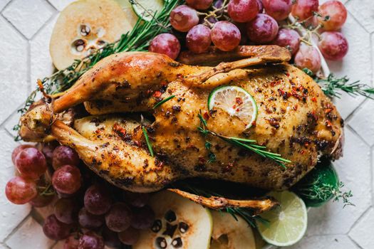 A duck baked for Thanksgiving as a symbol of family unification at a common holiday table. Still life in orange tones, shot in a light key on a white ceramic background. The atmosphere of the festival and celebration. The dish is decorated with grapes, lime, quince and aromatic herbs.