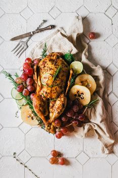 A duck baked for Thanksgiving as a symbol of family unification at a common holiday table. Still life in orange tones, shot in a light key on a white ceramic background. The atmosphere of the festival and celebration. The dish is decorated with grapes, lime, quince and aromatic herbs.