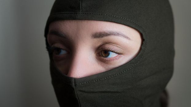 Female portrait of young girl wearing khaki balaclava, only eyes are visible, mandatory conscription, military, feminism, equality concept.