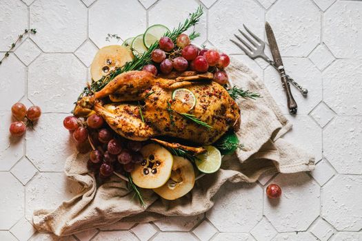 A duck baked for Thanksgiving as a symbol of family unification at a common holiday table. Still life in orange tones, shot in a light key on a white ceramic background. The atmosphere of the festival and celebration. The dish is decorated with grapes, lime, quince and aromatic herbs.